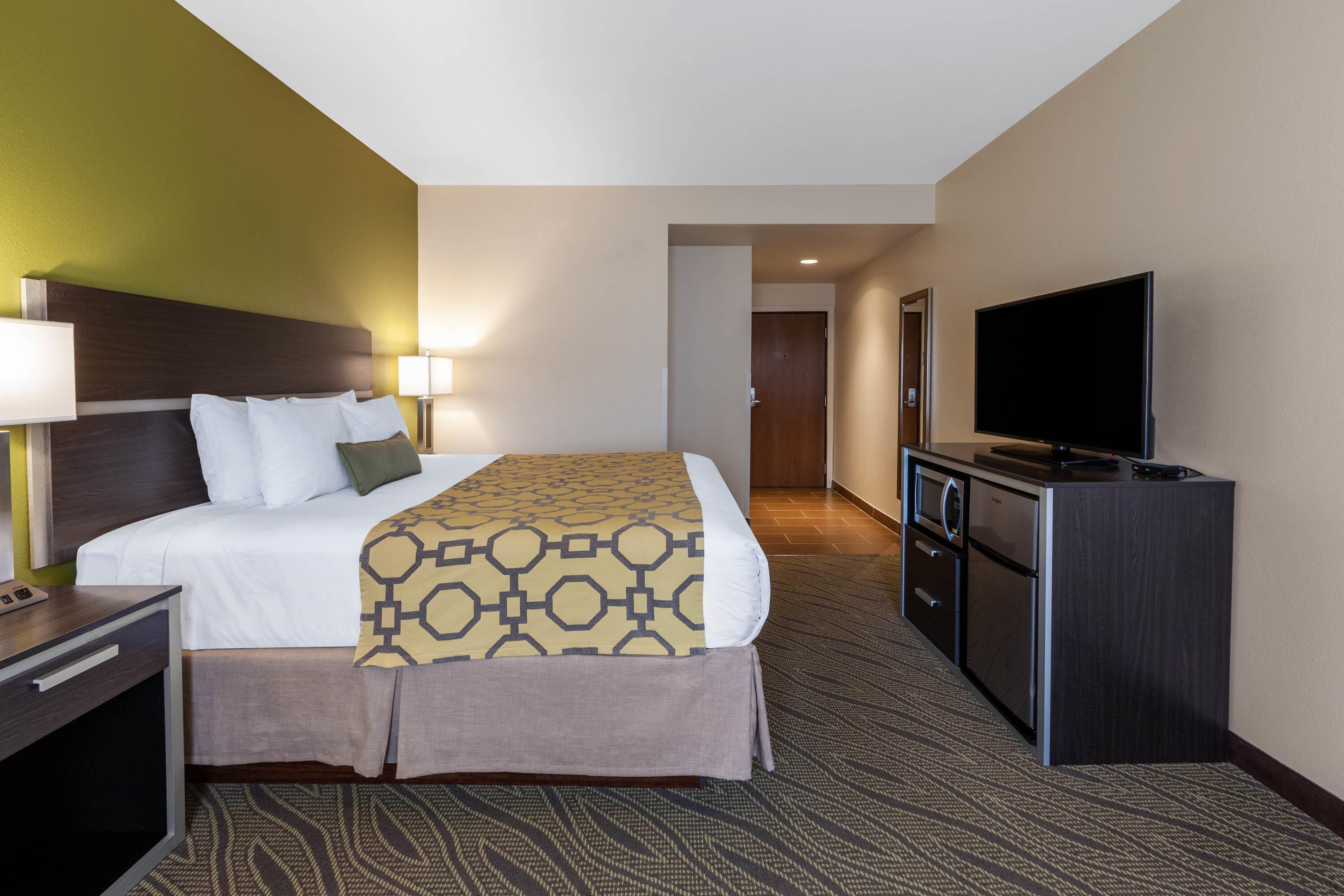 A hotel room with a bed, bedside table, lamp, TV, and a kitchenette.