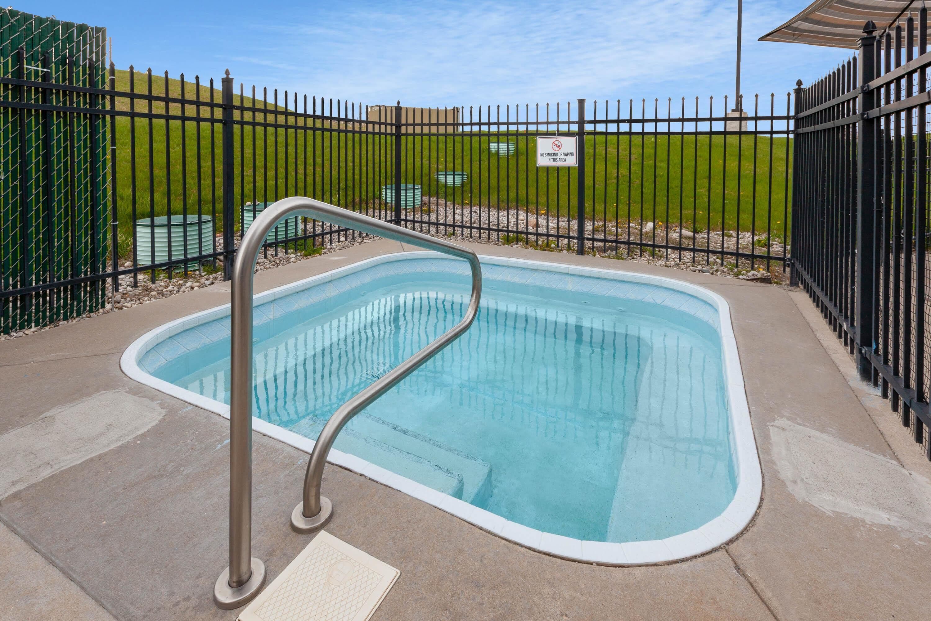 Piscina con scaletta in metallo, circondata da una recinzione nera e da un'area verde.