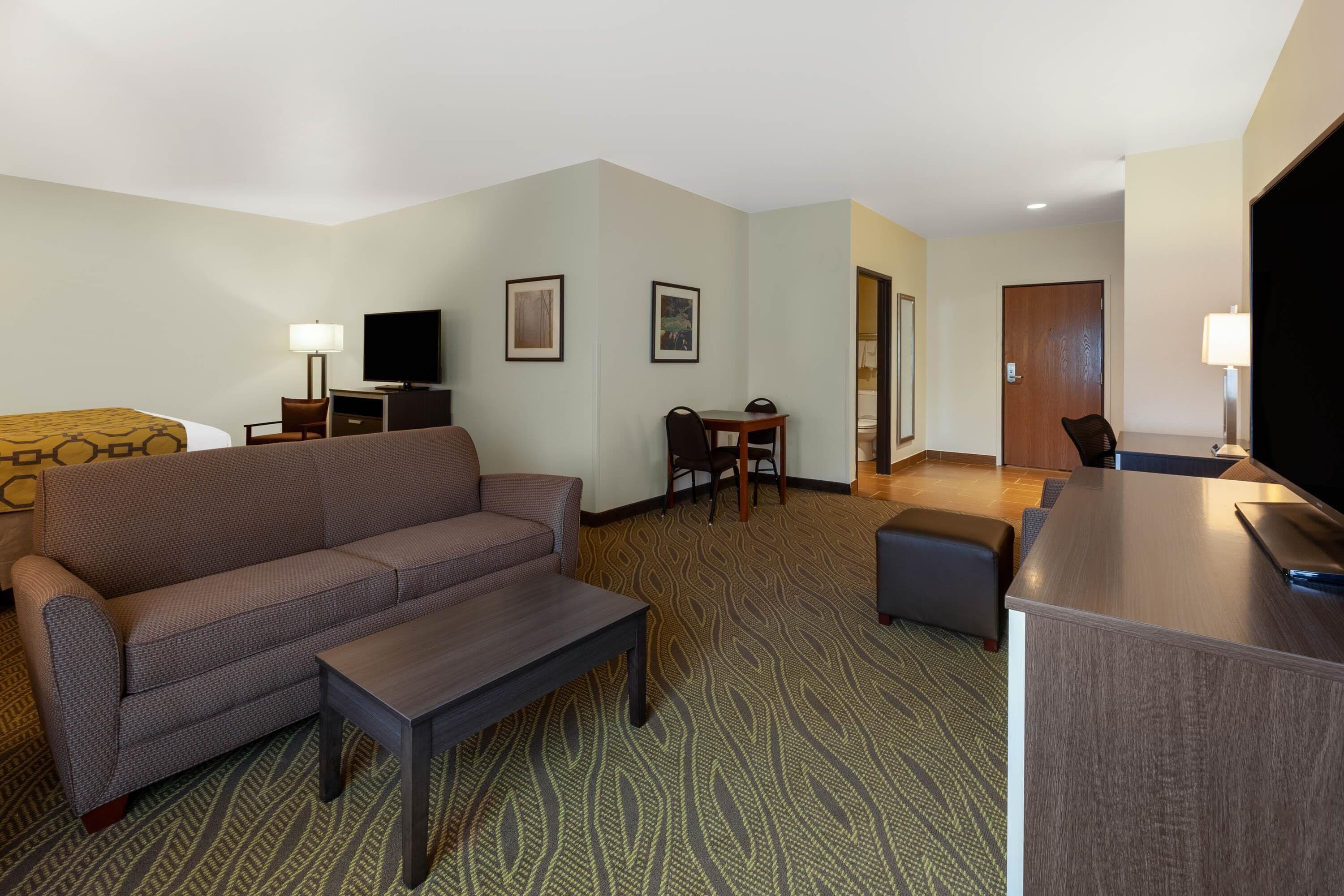 A hotel room with a sofa, a small table, a TV, a desk, and a chair.