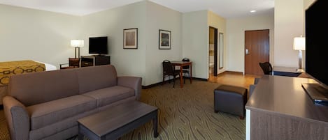 A hotel room with a sofa, a small table, a TV, a desk, and a chair.