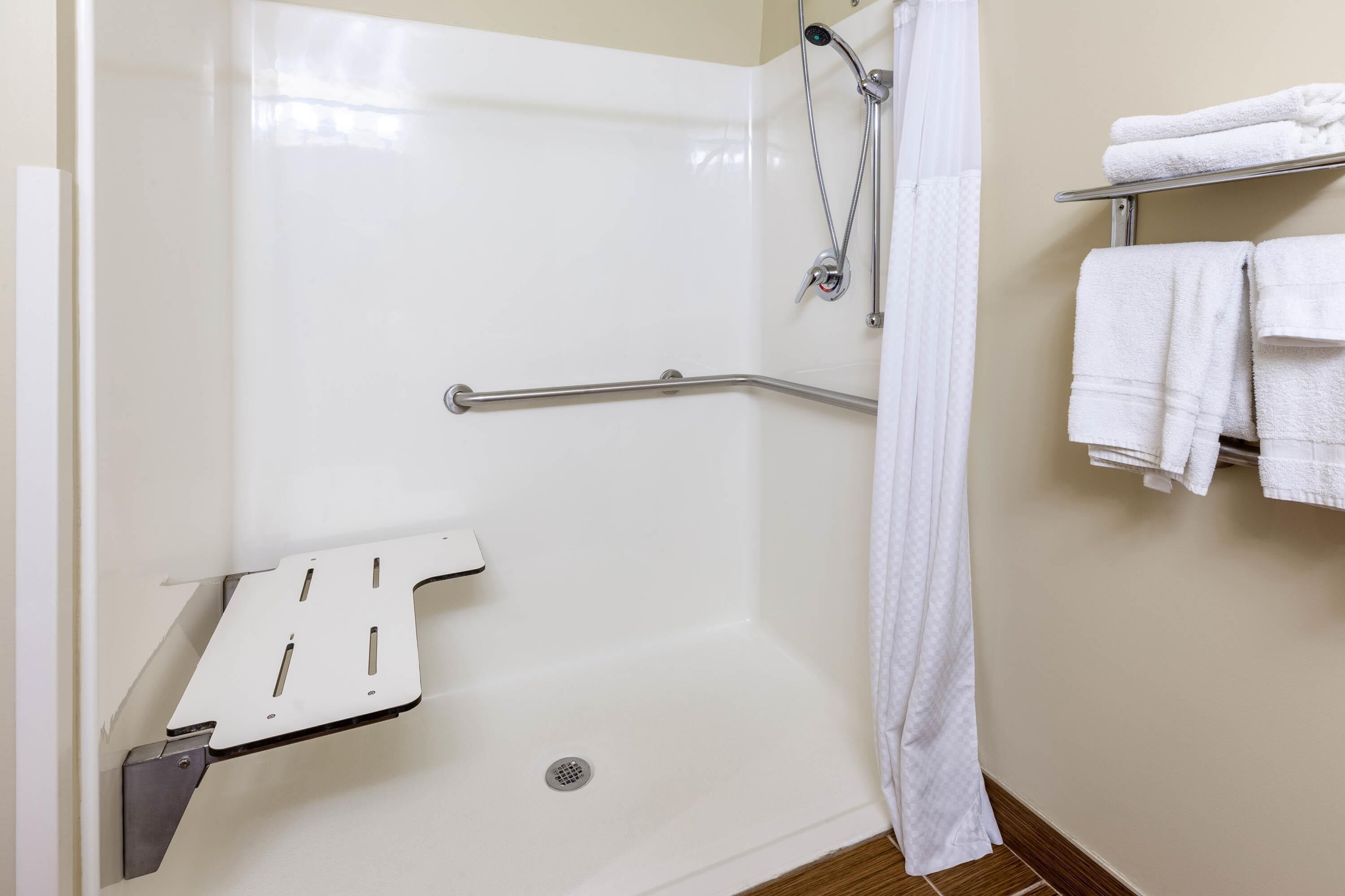 A bathroom with a walk-in shower, grab bars, a towel rack, and a white shower curtain.