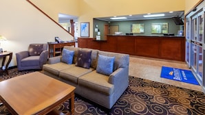 A hotel lobby with a sofa, armchair, wooden reception desk, and a carpeted floor. - Baymont by Wyndham Beulah (Beulah)