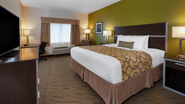 A hotel room with a large bed, a desk, a television, and a window with curtains. - Baymont by Wyndham Beulah (Beulah)