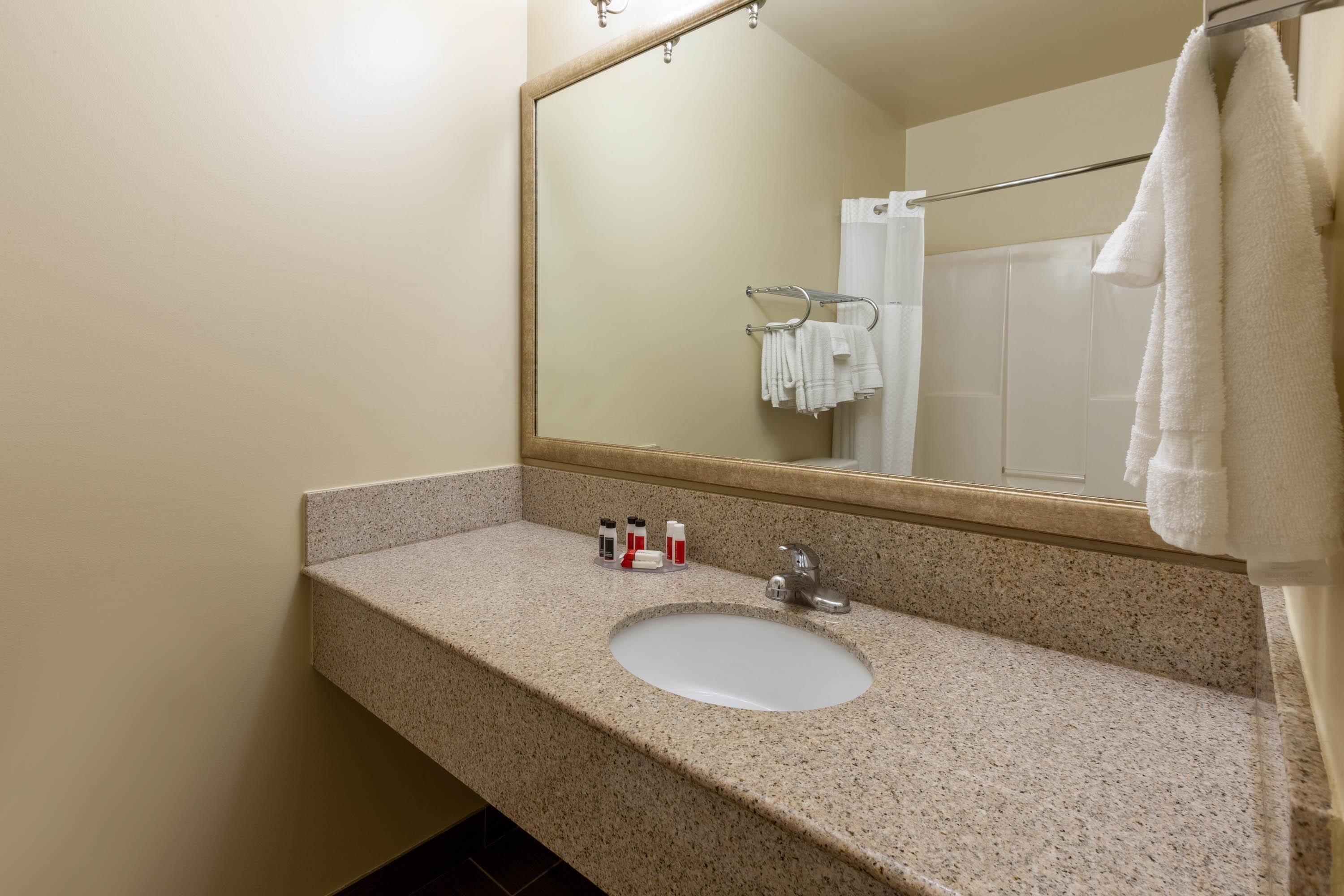 A bathroom with a granite countertop, a sink, a mirror, and a towel rack.