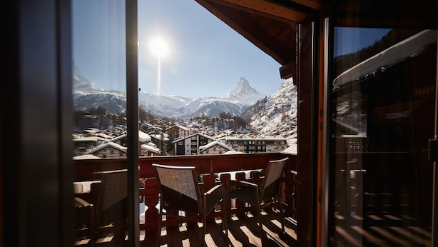 A balcony with wooden chairs and a view of snow-covered mountains and a prominent peak. - Hotel Ambiance  (Zermatt)
