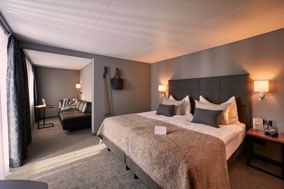 A modern hotel room with a large bed, a sofa, a desk, and a lamp.