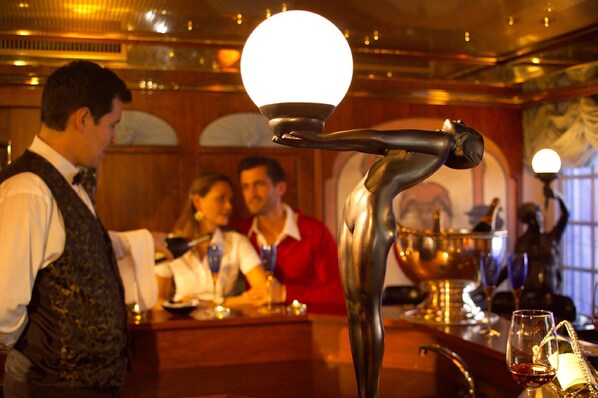 A bar area with a bartender, a polished bar counter, and a decorative light fixture.