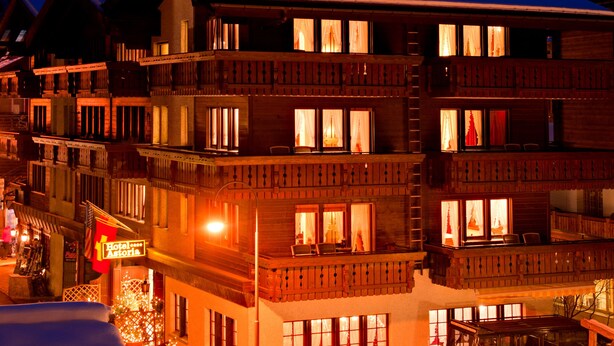 A multi-story hotel with balconies, a snow-covered ground, and a mountain in the background. - Hotel Astoria (Zermatt)