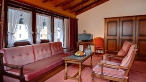 A cozy living room with a red sofa, wooden armchairs, a coffee table, and a television. - Hotel Astoria (Zermatt)
