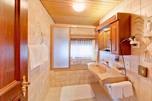 A bathroom with a wooden ceiling, a bathtub, a sink, and a mirror. - Hotel Astoria (Zermatt)