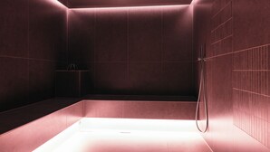 Un bany modern, amb il·luminació suau, amb un espai de dutxa de vidre i un plat de roba.