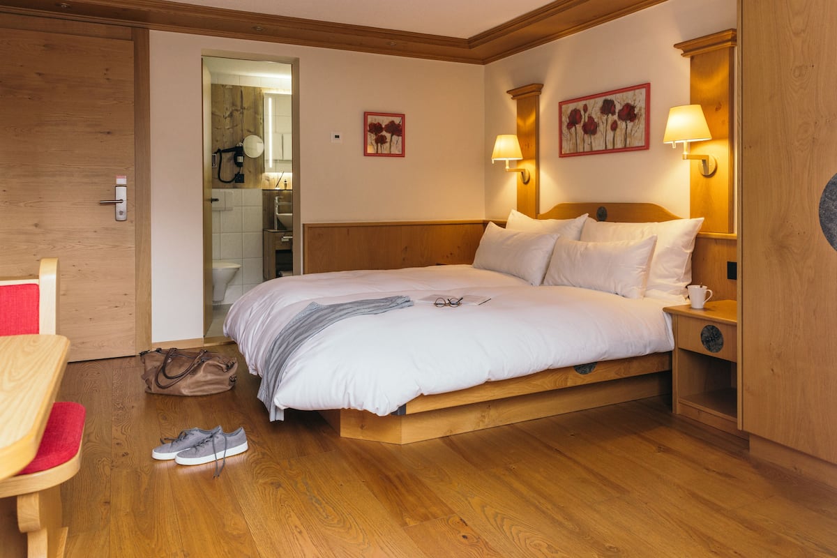 A neatly arranged hotel room with a wooden bed, bedside lamps, and a small table with a chair.