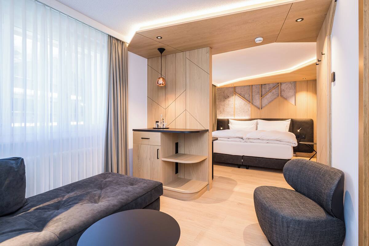 A modern hotel room with a bed, a desk, a sofa, and a small seating area.