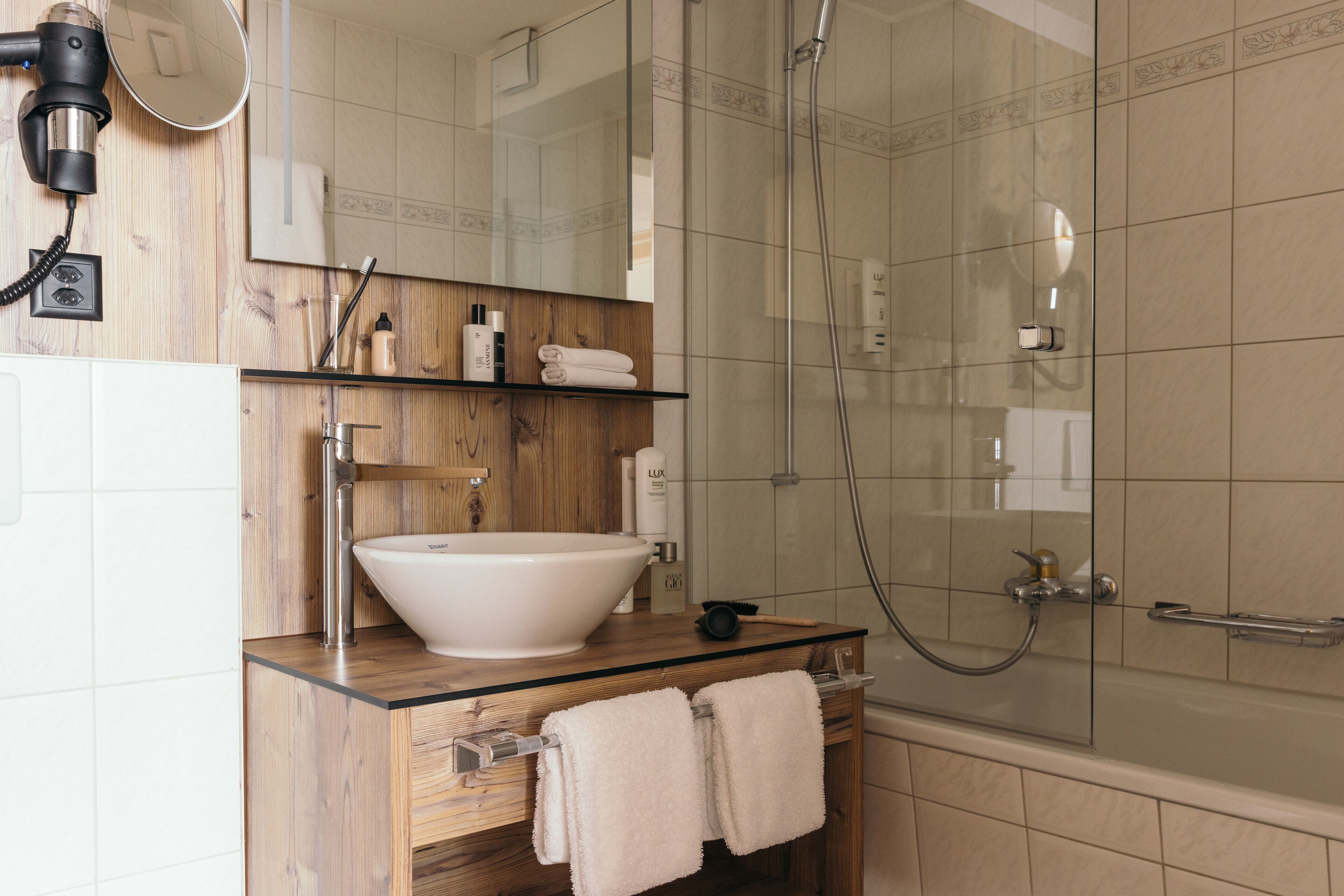 Un baño moderno con un lavabo blanco grande, cabina de ducha con mampara de vidrio y muebles de madera.