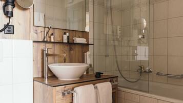 Un baño moderno con un lavabo blanco grande, cabina de ducha con mampara de vidrio y muebles de madera.