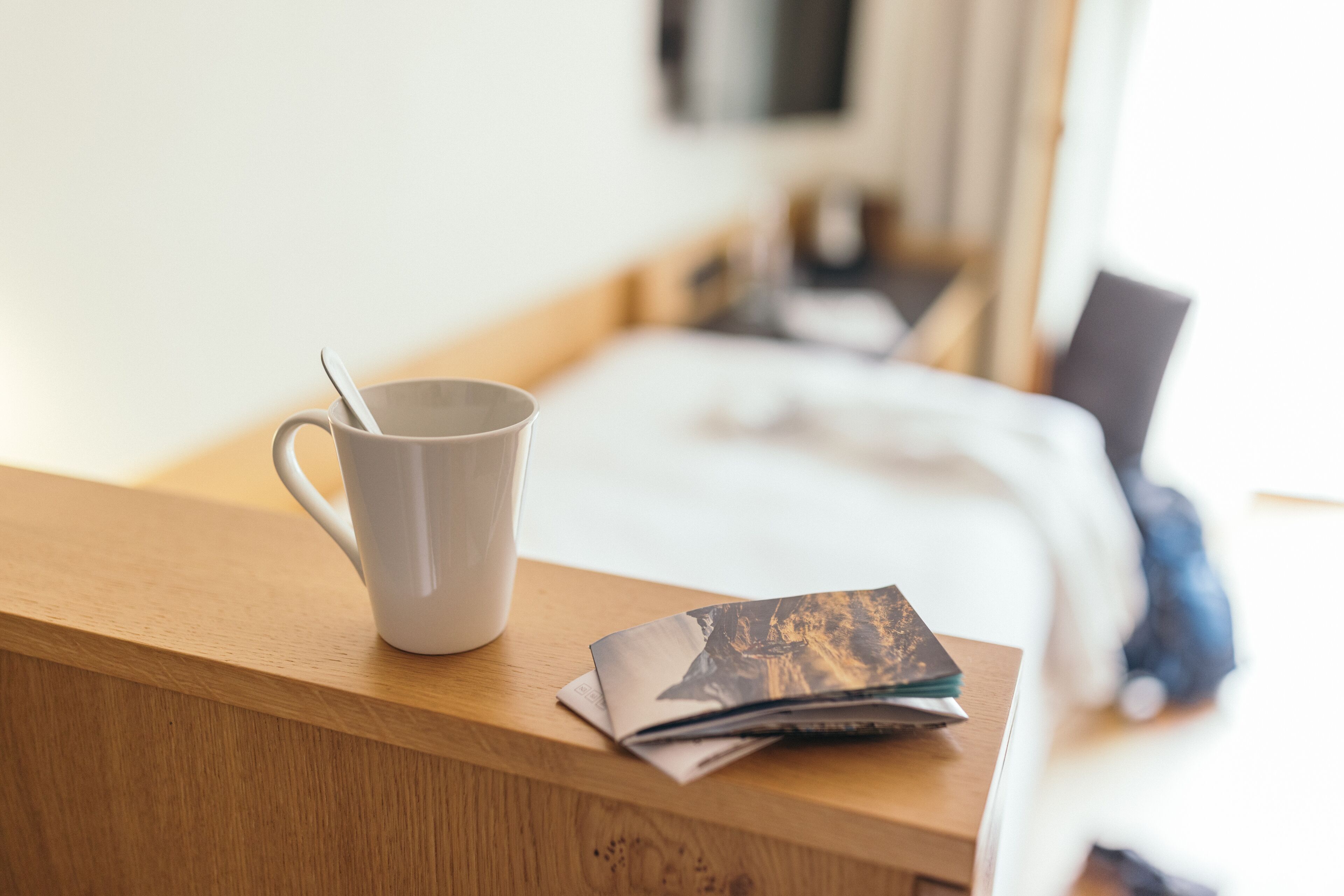 Una mesita de noche de madera con una taza blanca y una revista.