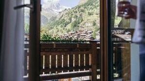 Vista des d'una finestra amb un balcó de fusta, sobre un poble de muntanya amb cases tradicionals i un cel serè.