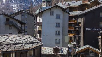 A traditional European village with stone buildings, a church tower, and a snow-covered mountain in the background.