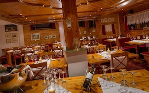 Un restaurante con interiores de madera, varias mesas dispuestas con copas de vino y velas, y un reloj grande sobre una columna.