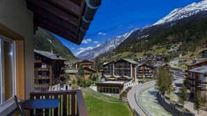 A mountain town with wooden buildings, a river, and snow-capped mountains in the background. - Hotel Excelsior (Zermatt)