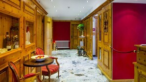 A room with wooden paneling, a red wall, a marble floor, a dining table with chairs, and a radiator. - Hotel Excelsior (Zermatt)