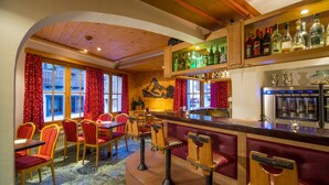 A cozy bar area with wooden furniture, a wine cooler, and a view of the street through large windows. - Hotel Excelsior (Zermatt)