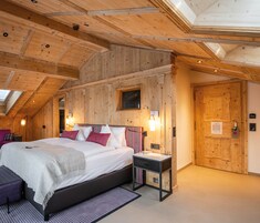 A bedroom with a wooden ceiling, a bed with white bedding, a nightstand, and a window.