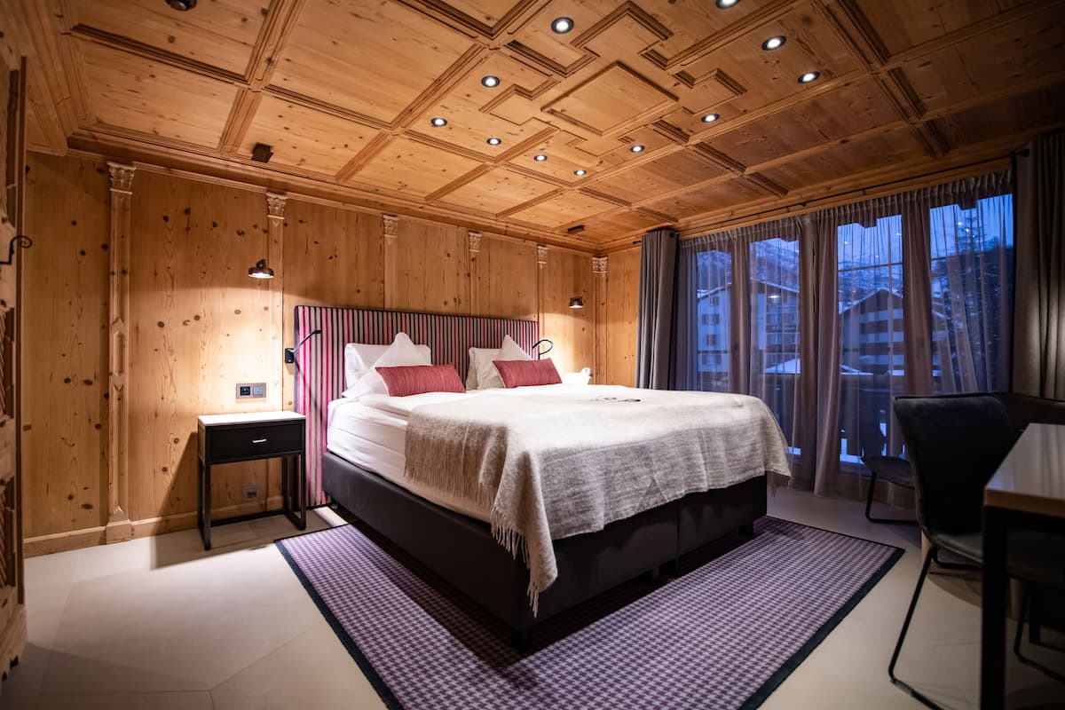 A wooden-paneled bedroom with a bed, bedside tables, and a view of the outside through large windows.