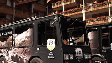 A black bus with "Hotel Alpenhof" and "Hotel Daniela" logos, parked in front of a building with balconies.