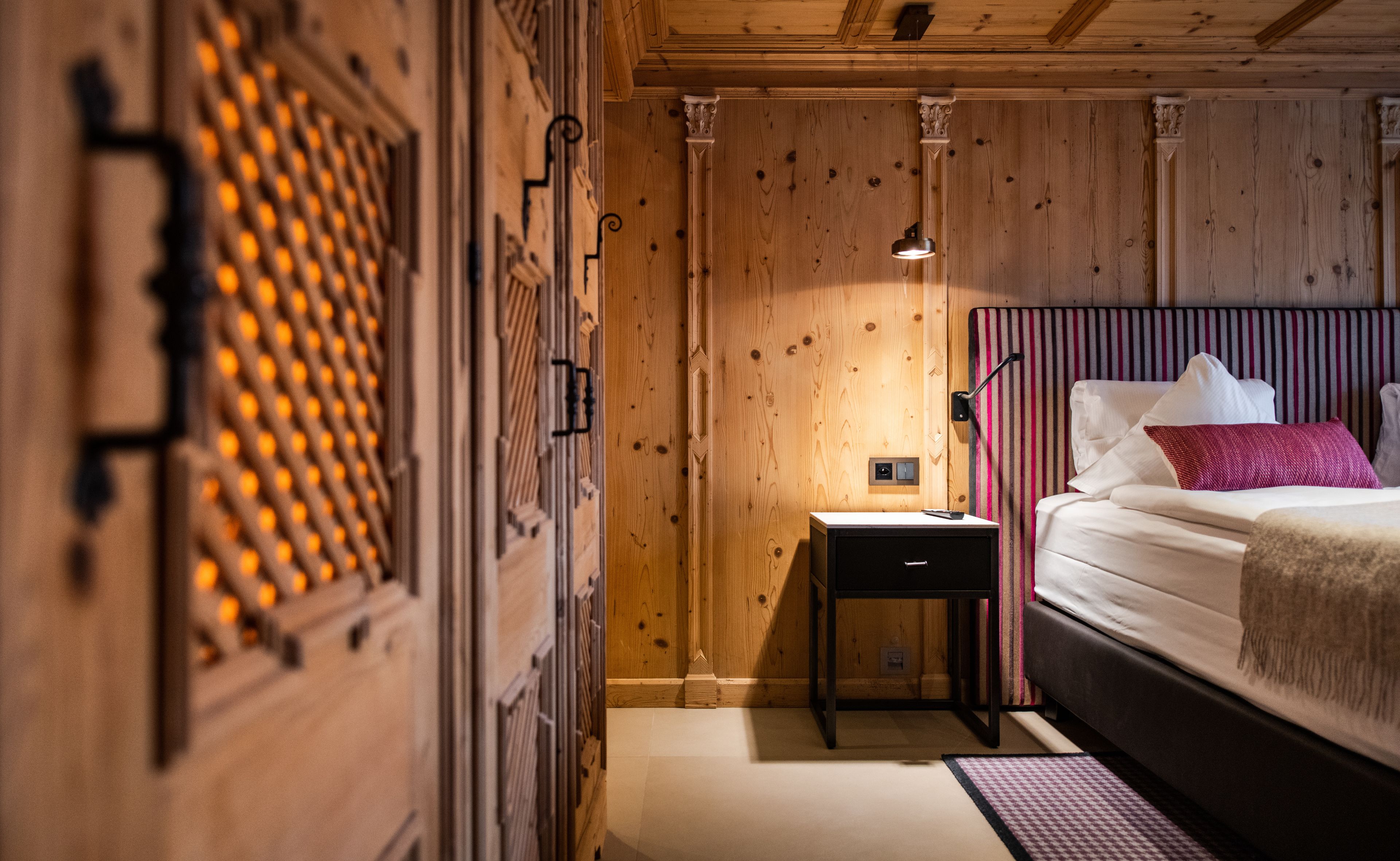 A wooden-paneled room with a bed, bedside table, and a wall-mounted light fixture.