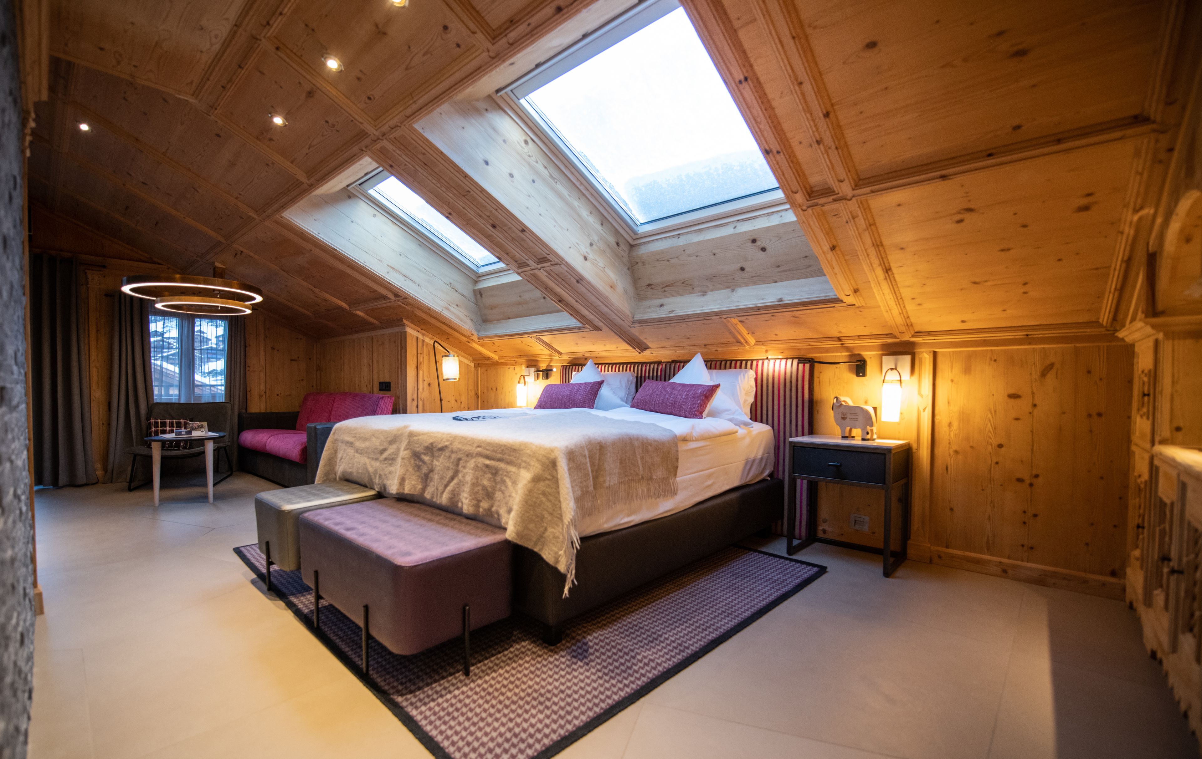 A bedroom with a skylight, a bed with pillows, a bedside table, and a small desk with a chair.