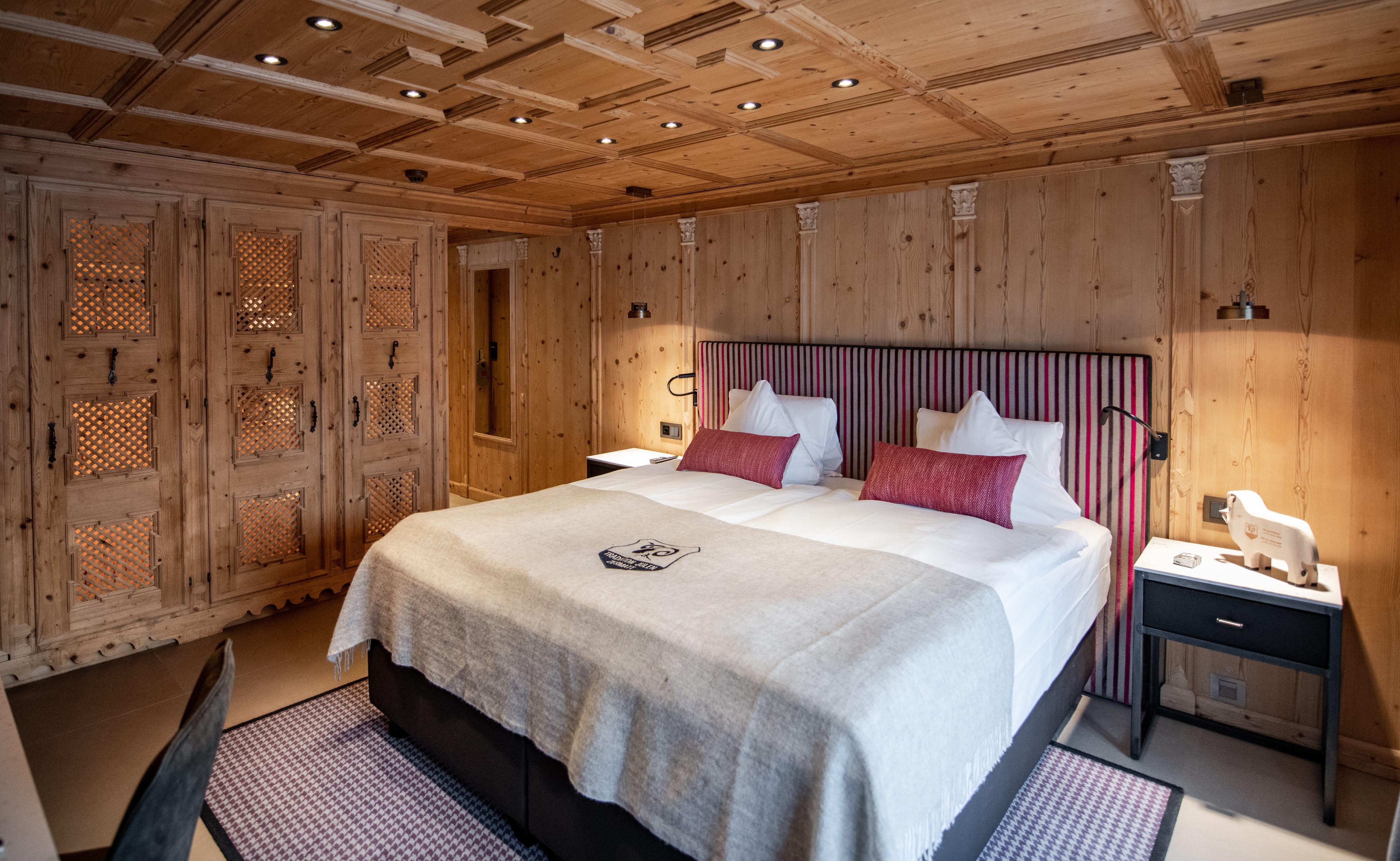 Un dormitorio con paneles de madera, una cama grande, dos mesitas de noche y una mesilla.
