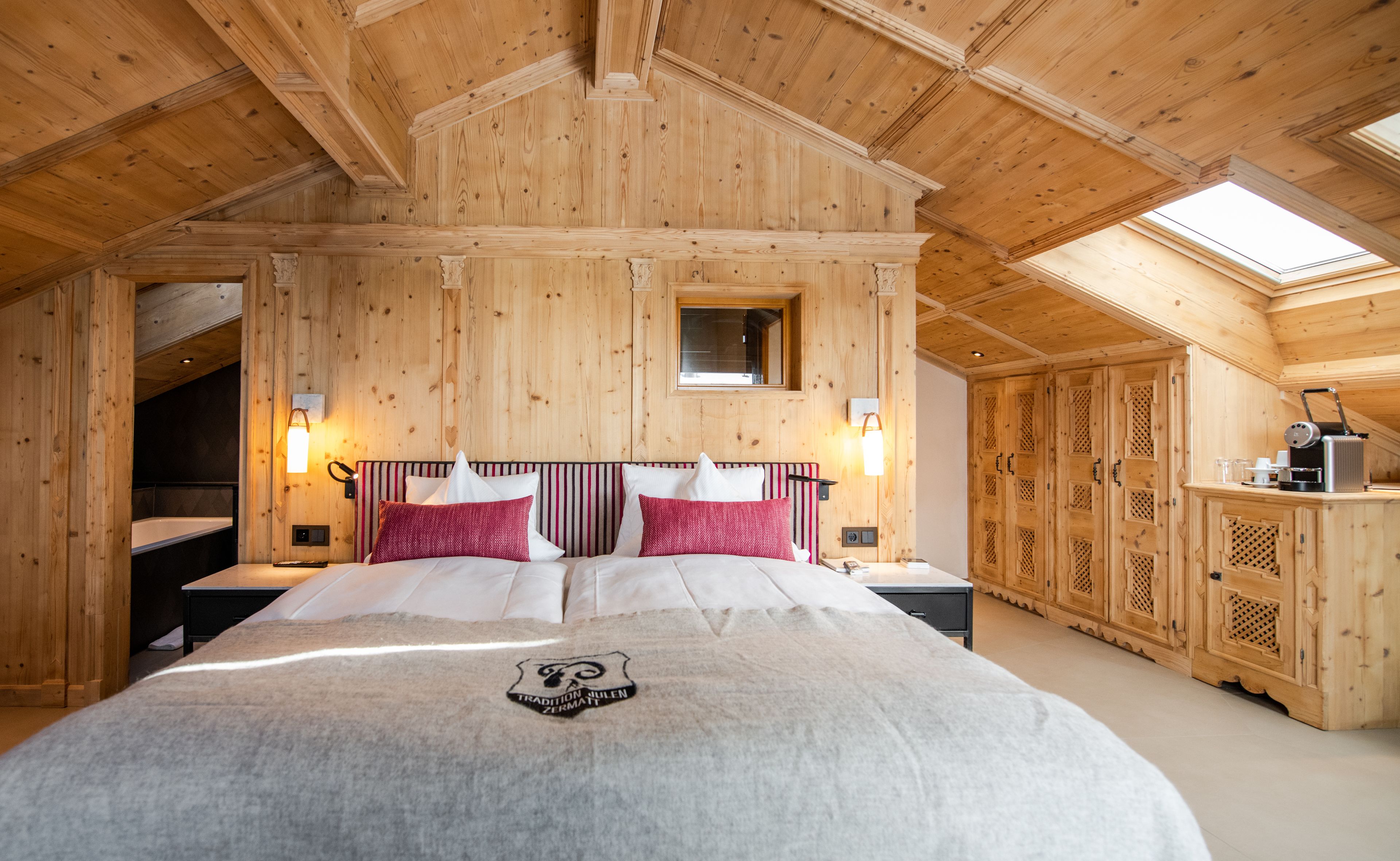 Una habitación de madera con una cama, un ventanal pequeño y una escalera.