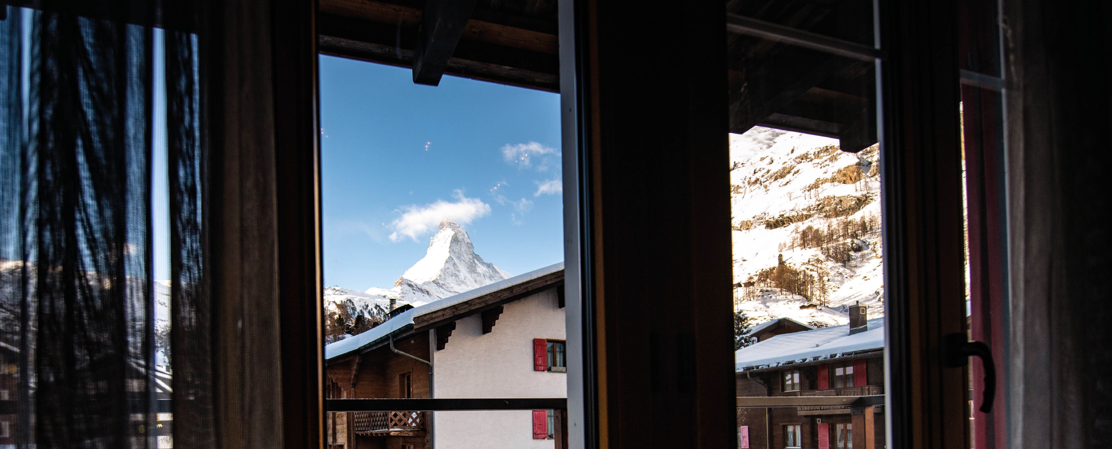A mountain view through a window with a chalet-style building in the foreground.