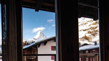 A mountain view through a window with a chalet-style building in the foreground.