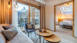 A modern hotel room with a sofa, a chair, a round table, and a bed. The room has large windows with a mountain view. - Resort La Ginabelle (Zermatt)
