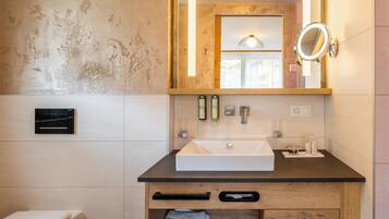Ein Badezimmer mit weißem Waschbecken, Holzkommode, einem Spiegel mit Beleuchtung und einem Handtuchhalter.