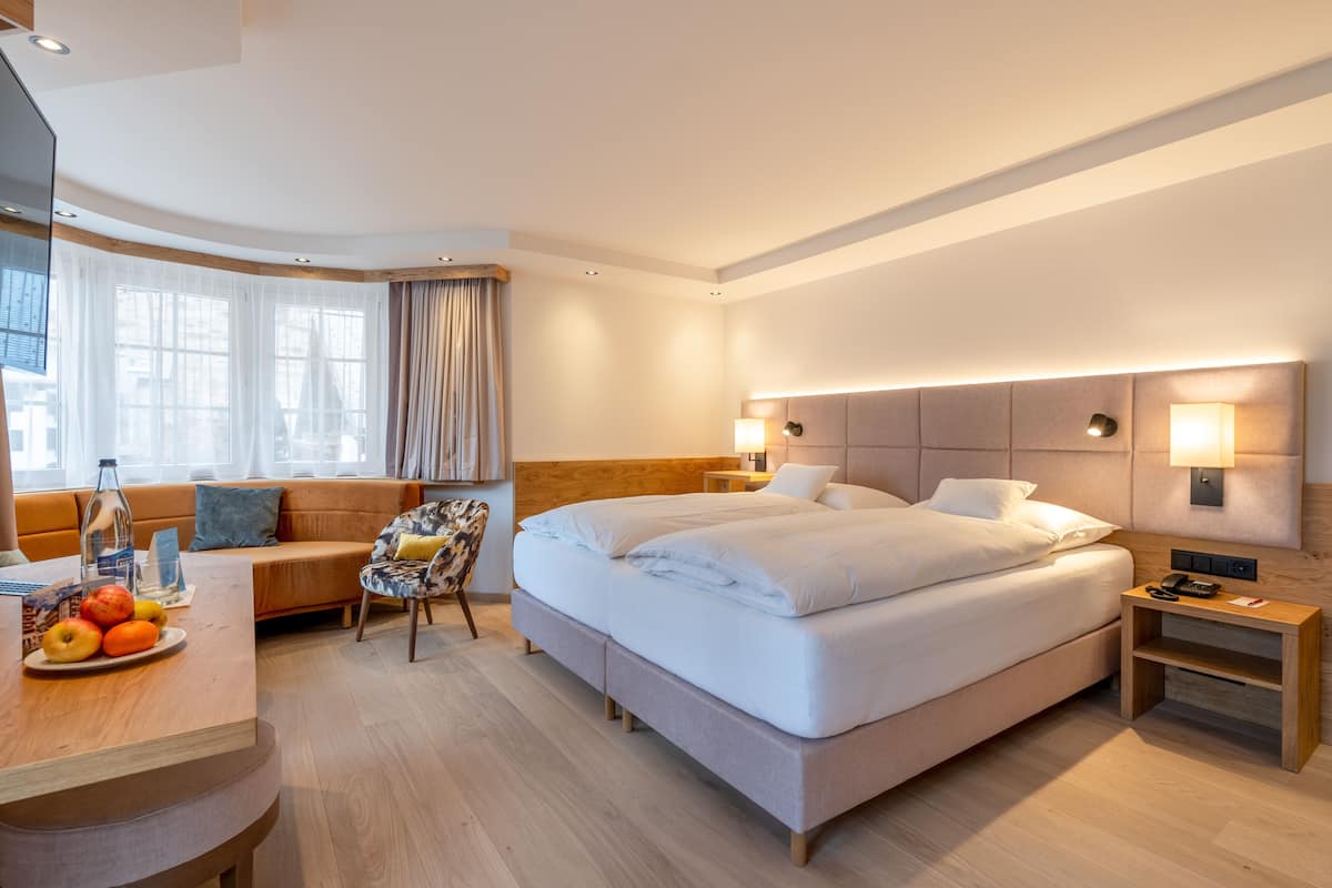 Ein Hotelzimmer mit einem großen Bett, einer Couch, einem Schreibtisch mit Obst und einem Sessel.