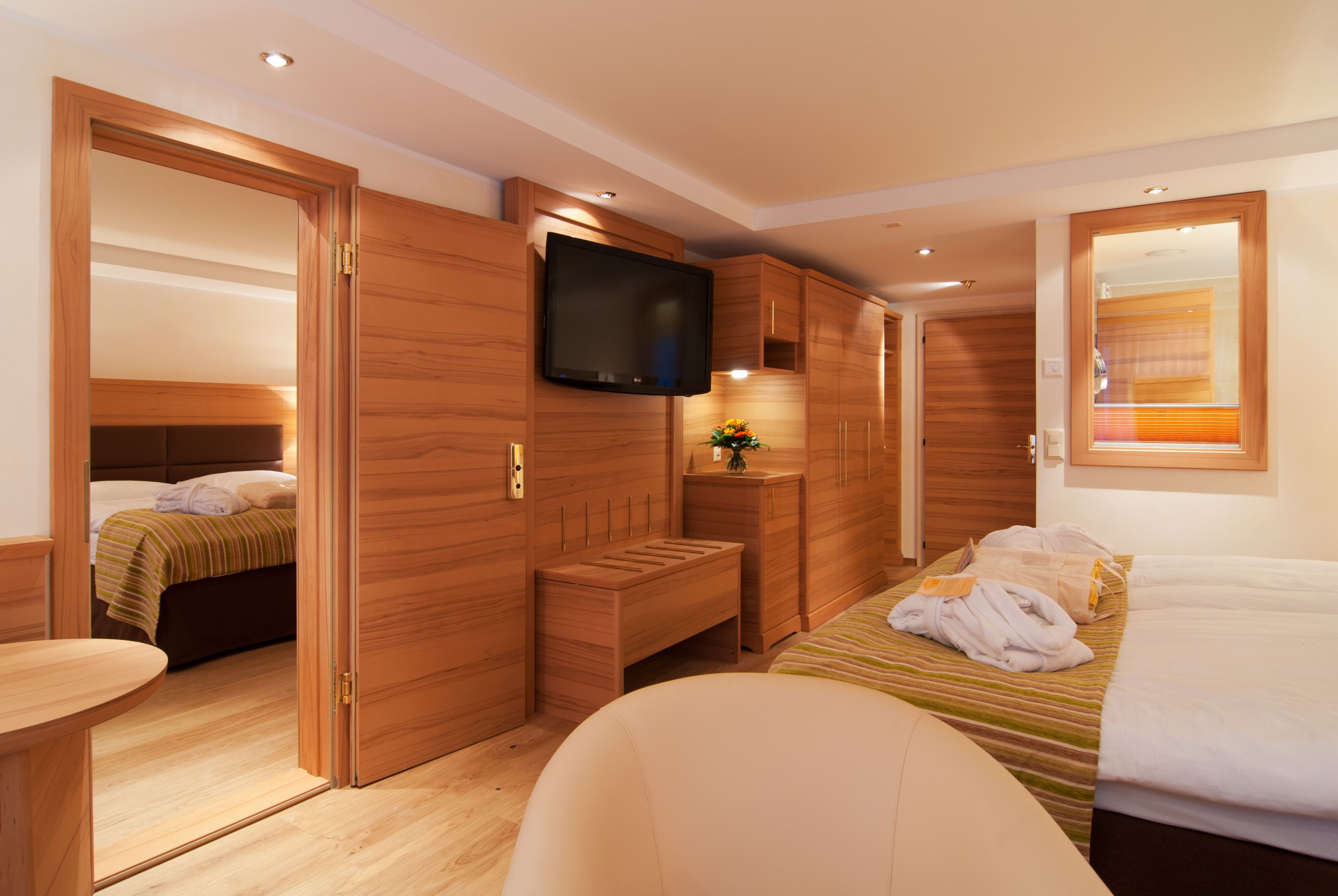 Una camera d'albergo moderna con arredi in legno, una televisione a schermo piatto, un letto con coperta a righe e una piccola panca di legno.