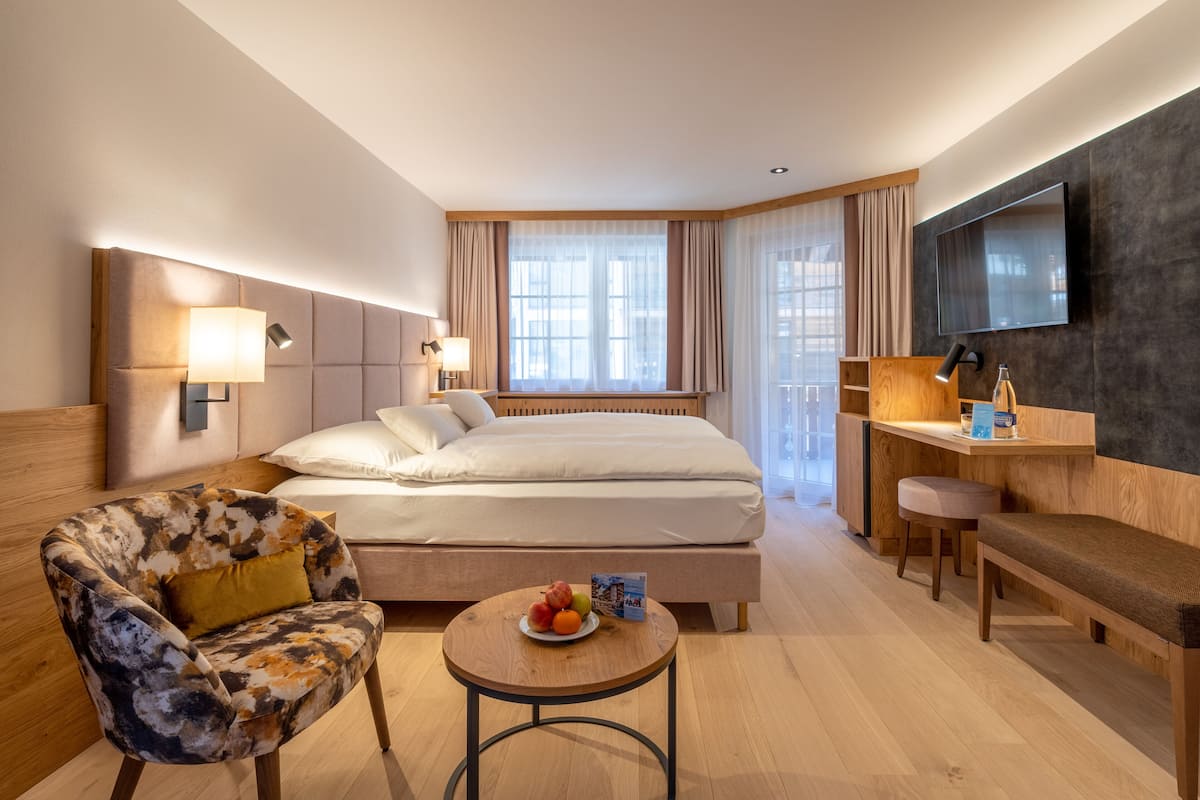 Ein modernes Hotelzimmer mit einem großen Bett, einem Schreibtisch, einem Stuhl und einem runden Tisch mit Obst.