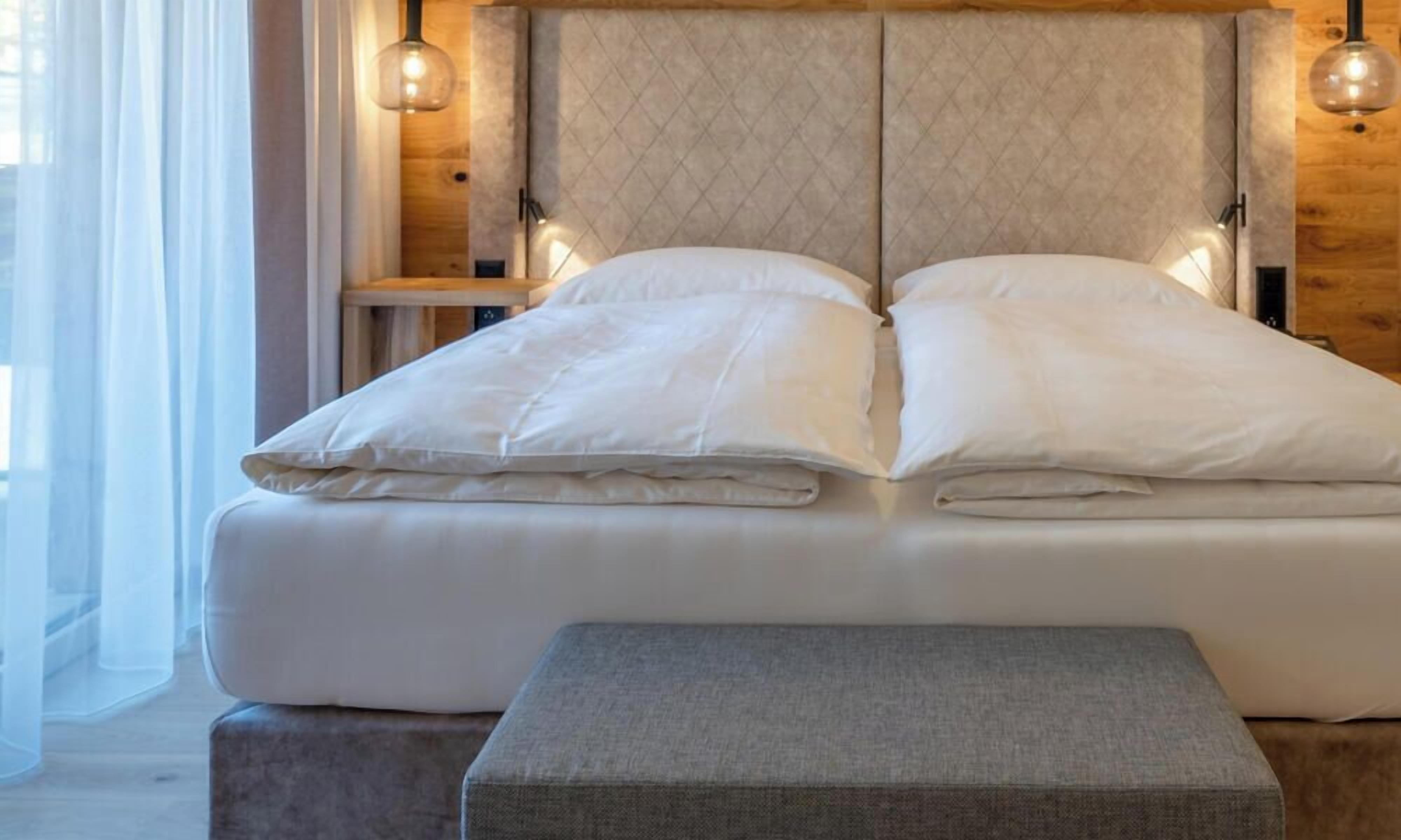 A bed with a quilted headboard, two bedside lamps, and a bench at the foot of the bed.