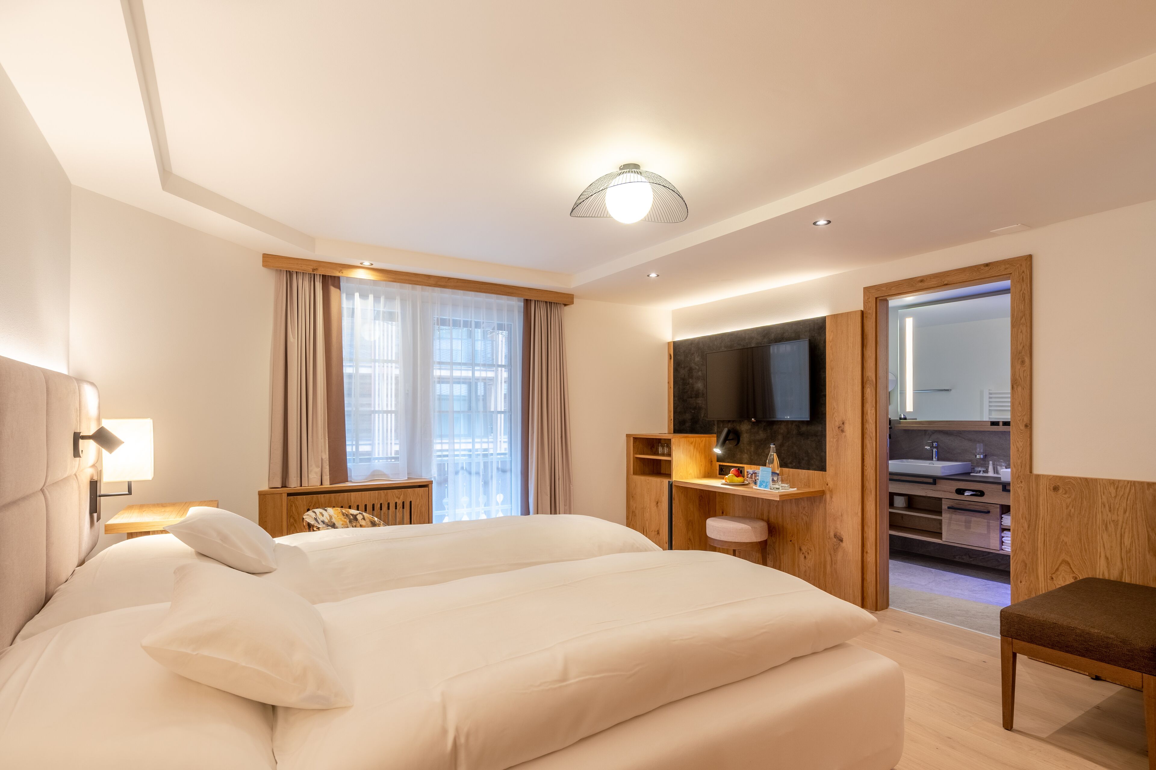 Habitación de hotel con una cama grande, un escritorio con computadora, una televisión y un baño visible a través de una puerta abierta.