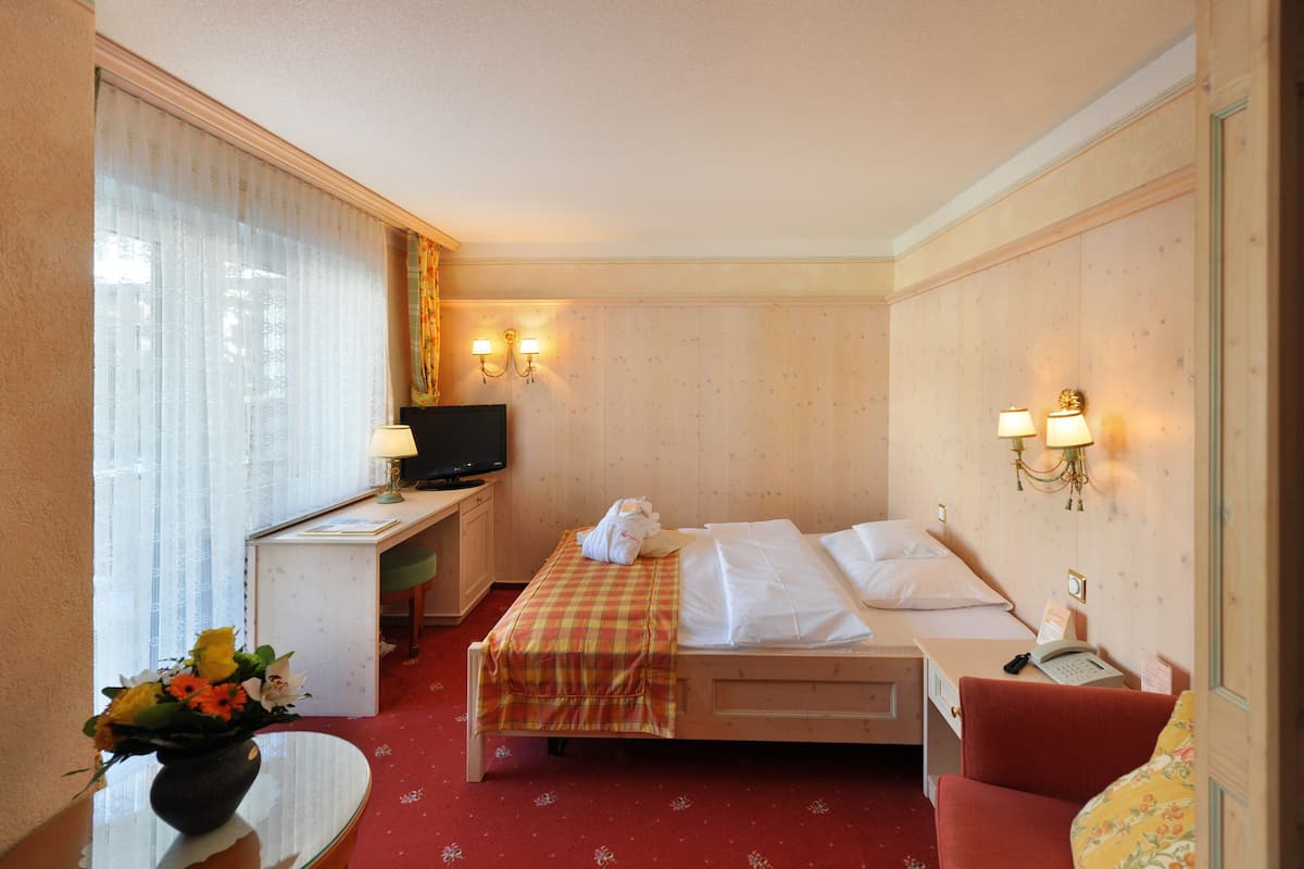 Ein Hotelzimmer mit Bett, Schreibtisch mit Fernseher, Stuhl und einem kleinen Tisch mit Blumenvase.