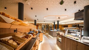 A modern breakfast buffet with wicker baskets of bread and pastries, wooden counters, and a clean, spacious layout. - Resort La Ginabelle (Zermatt)