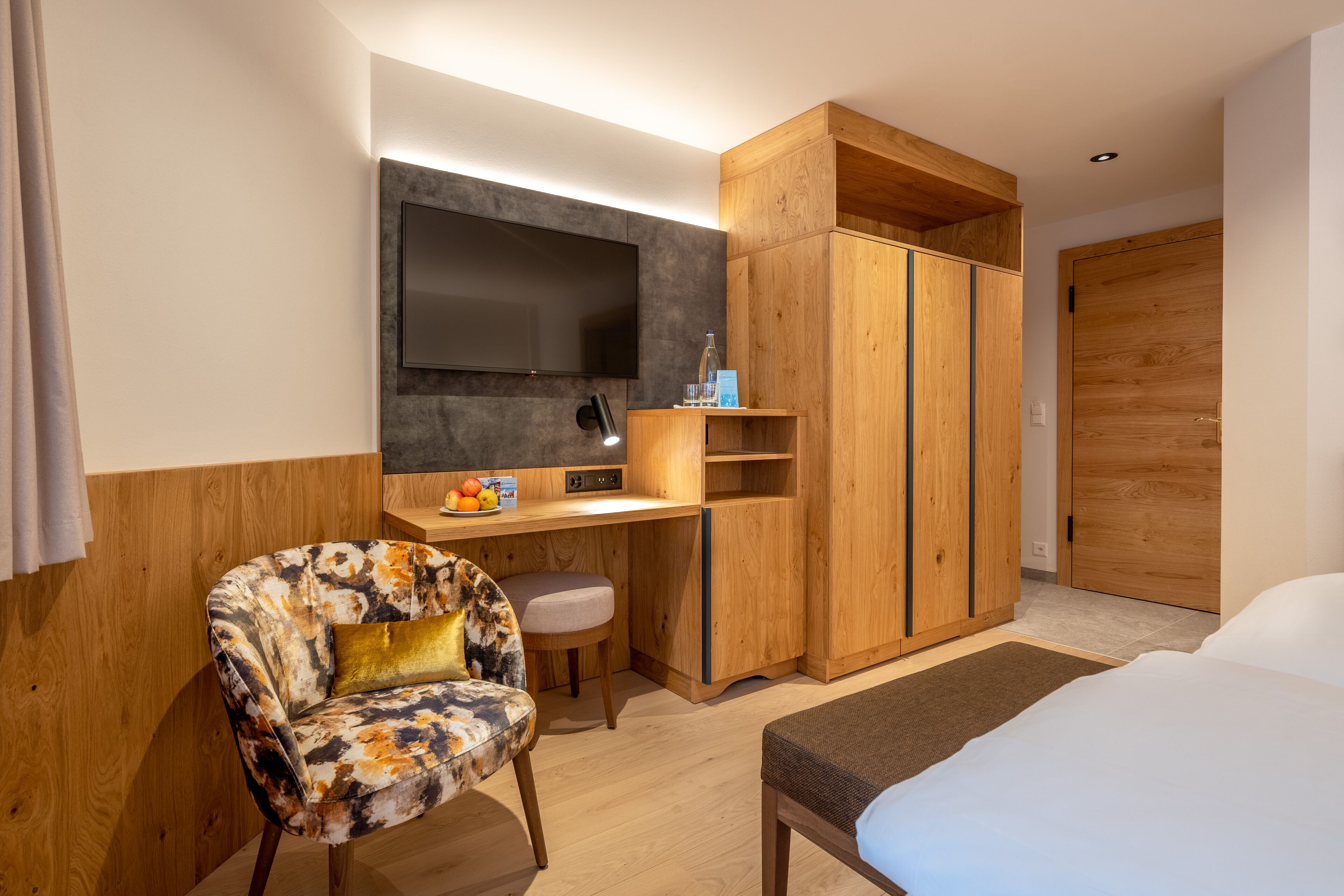 Ein modernes Hotelzimmer mit einem Holztisch, einem bequemen Sessel, einem Bett und einem Kleiderschrank.