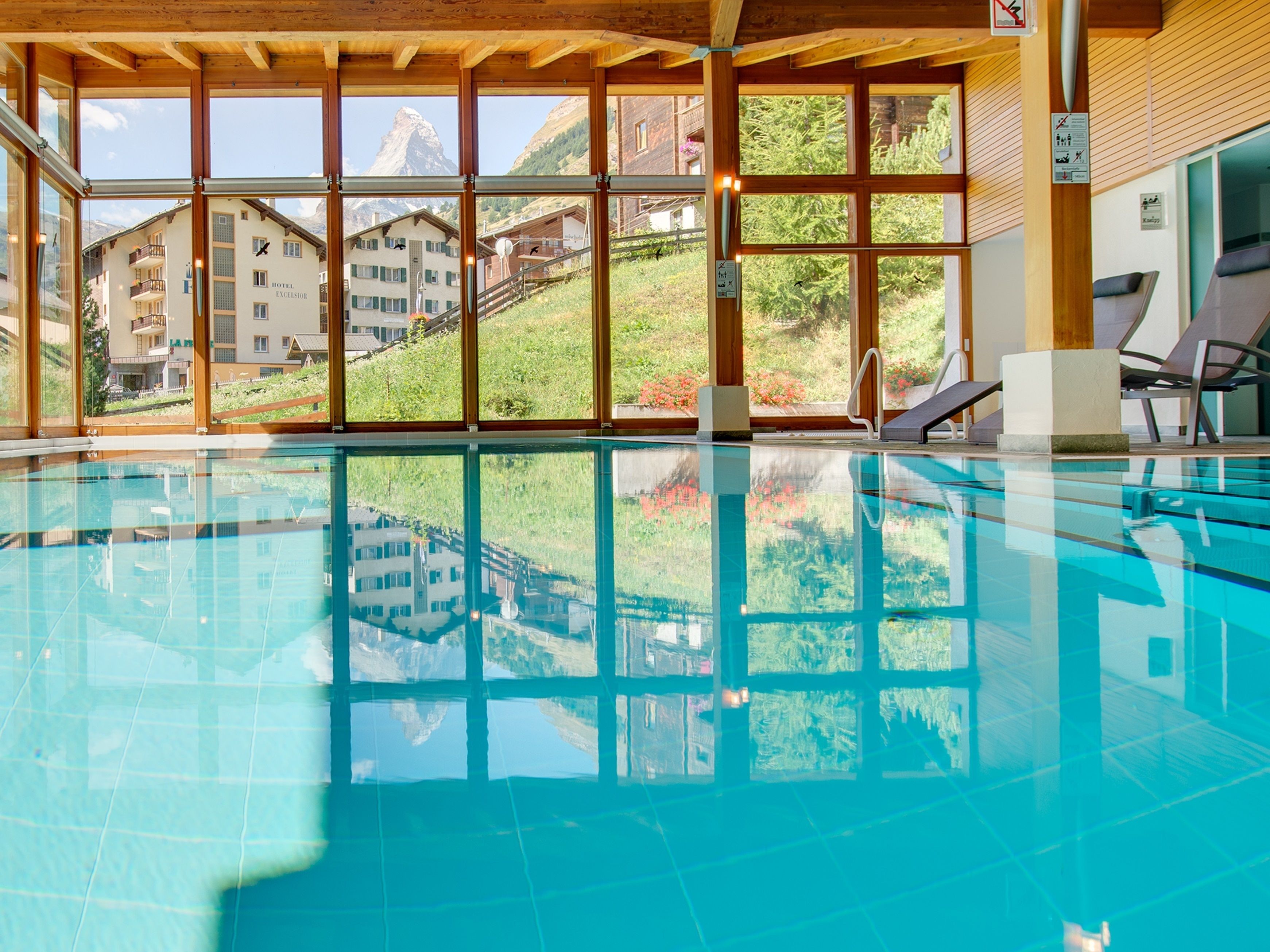 A swimming pool with clear blue water, large windows offering views of a mountainous landscape, and a wooden ceiling.