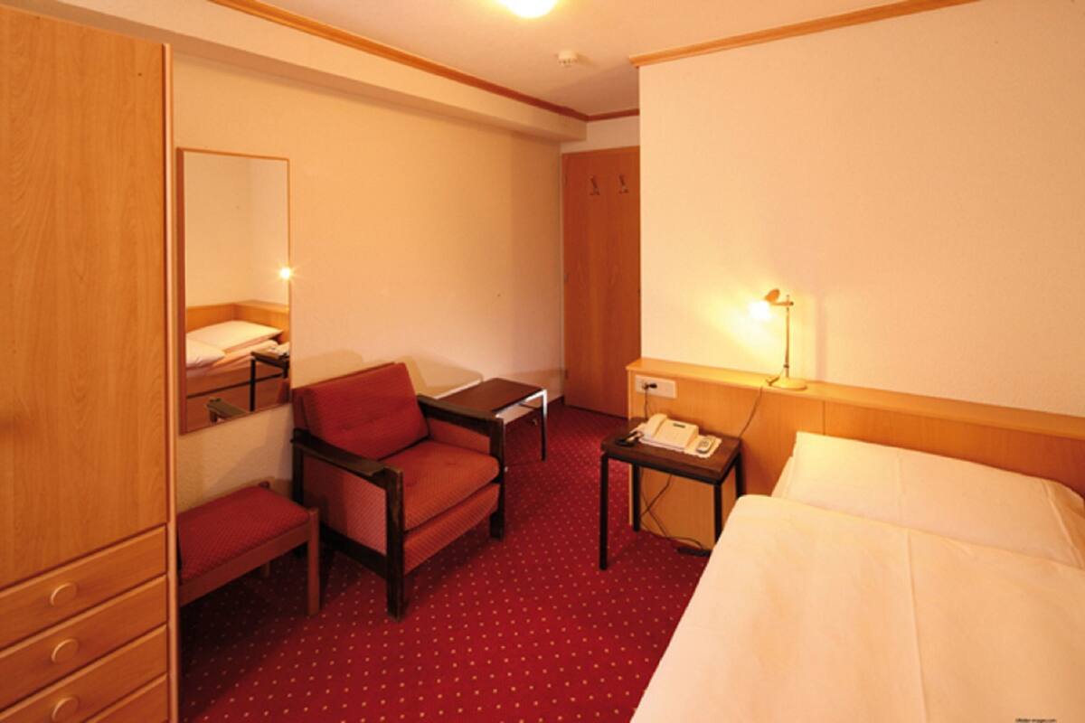 A hotel room with a bed, a desk, a chair, a small table, a telephone, a mirror, and a wardrobe.