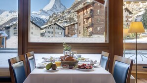 Una mesa de comedor con alimentos para el desayuno, vistas de montañas nevadas y arquitectura de madera.