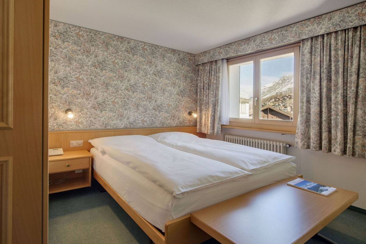 A hotel room with a bed, bedside table, and a window with curtains.
