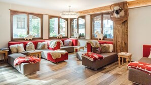 A cozy, well-lit room with large windows, a wooden ceiling, and a variety of seating options including sofas and a bench. - Hotel Daniela (Zermatt)